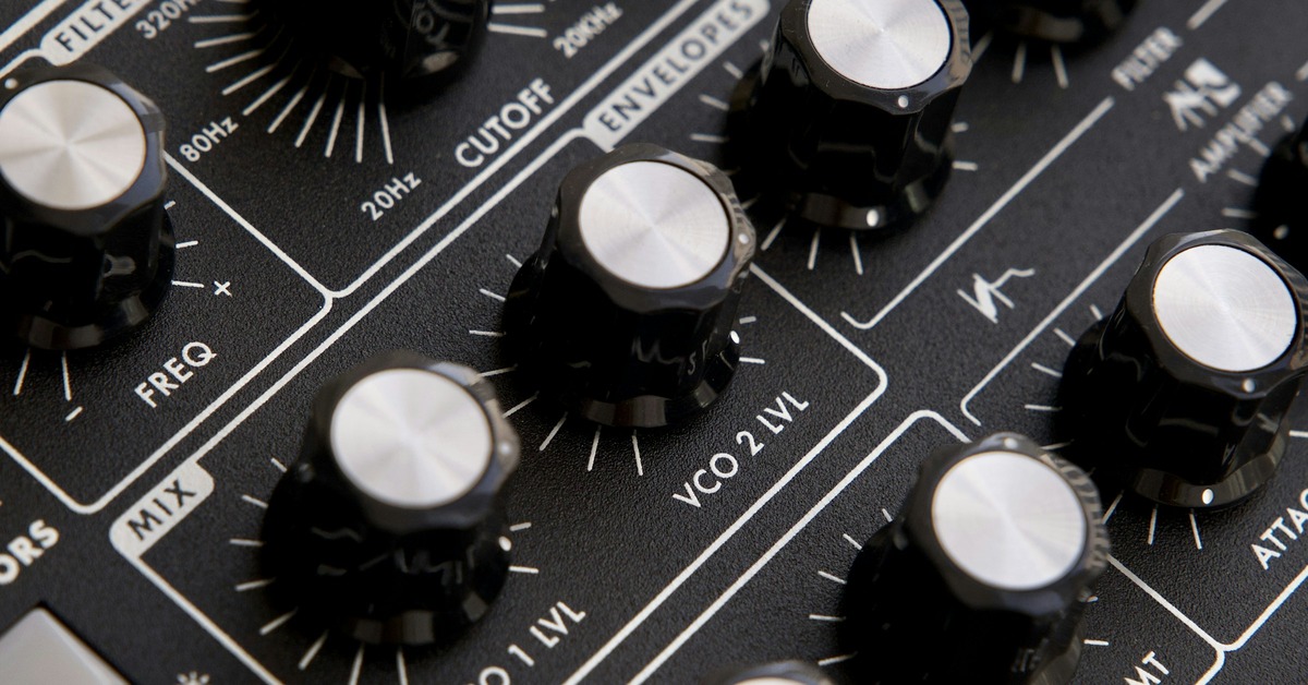 Close up of an analog synthesizer with patch cables, knobs, and faders in a dimly lit studio