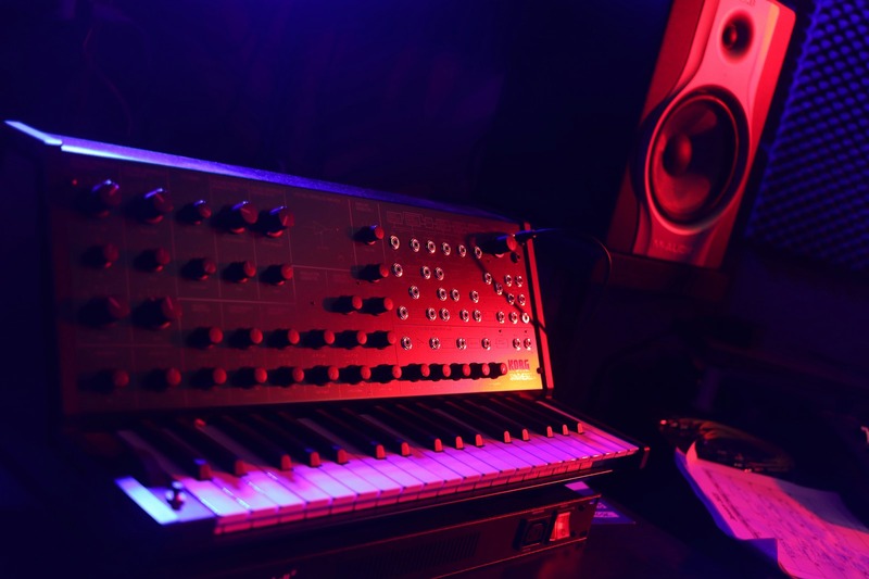 A desktop music production setup with a small synthesizer, audio interface, and studio headphones