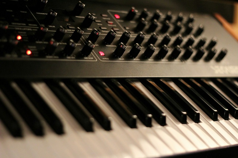 A modern digital synthesizer with a keyboard and backlit display on a desk in a music studio