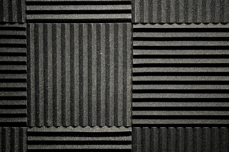 Black acoustic foam tiles mounted on the inside of a DJ booth panel for sound treatment and feedback control