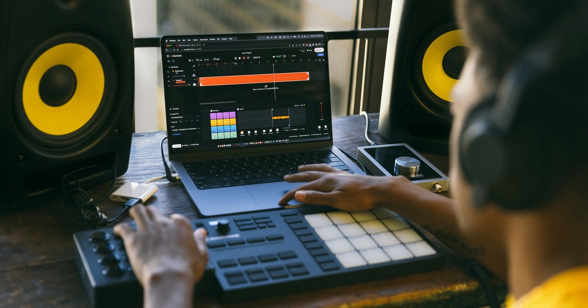 A DJ controller placed on a table next to a laptop in a home studio setup with headphones and speakers