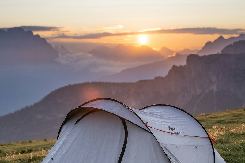 Assorted camping gear including a small tent, sleeping bag, and camping chair arranged on green grass