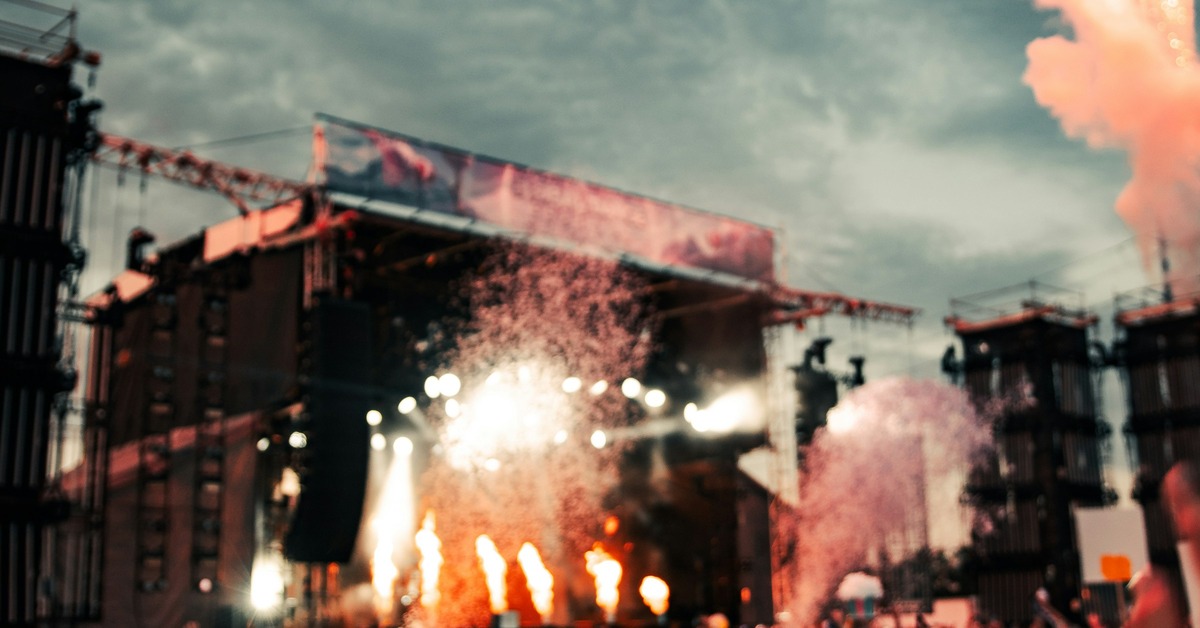 A large crowd of electronic music fans in front of a lit stage at sunset