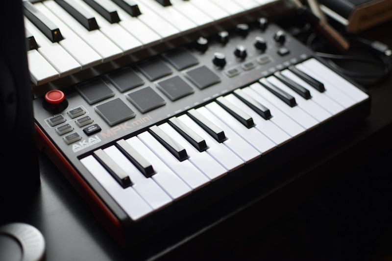 MIDI controller keyboard with knobs and pads on a desk next to a laptop running music production software
