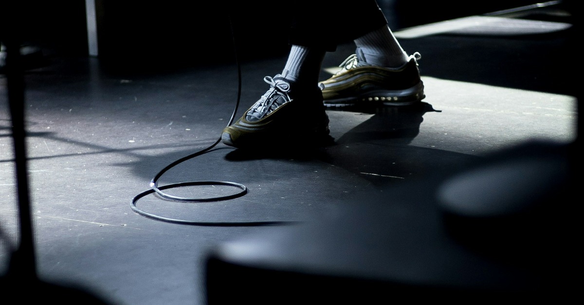Musician performing on stage with a MIDI foot controller at their feet during a live show