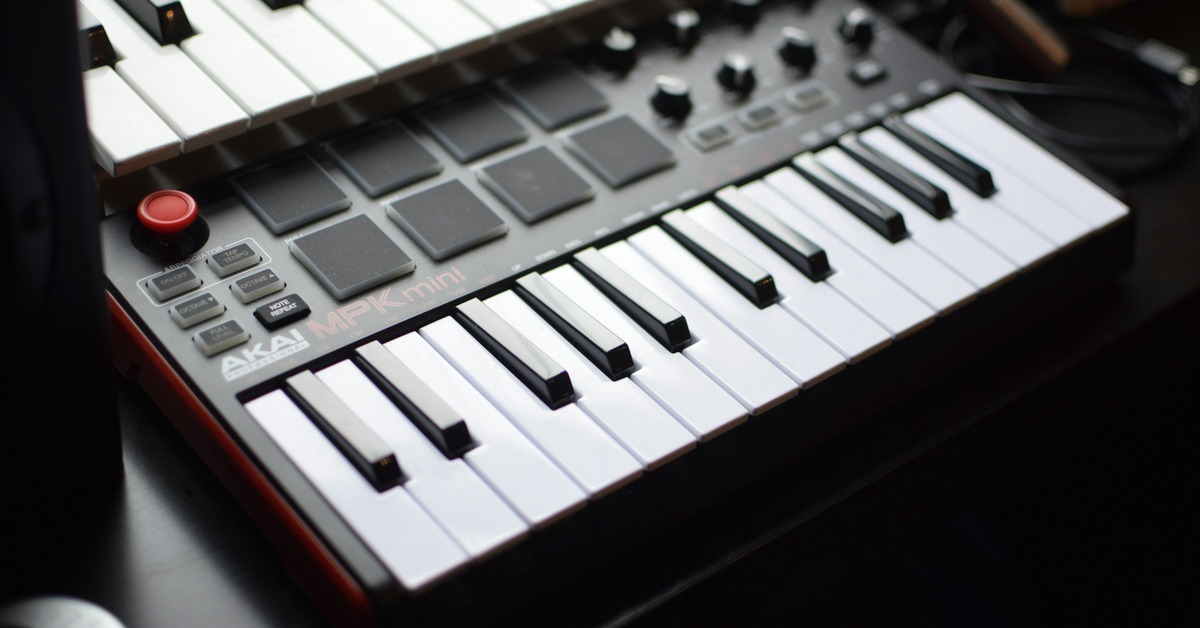 A producer's hands playing a MIDI keyboard controller in a home studio setup