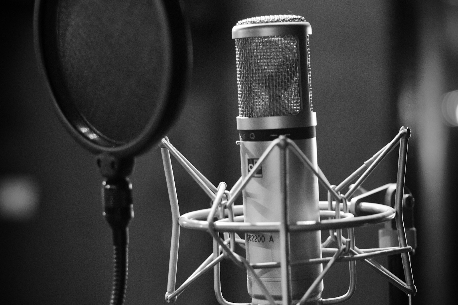 A producer in a recording room holding a cheap dynamic microphone next to an expensive condenser microphone on a stand, comparing the two.