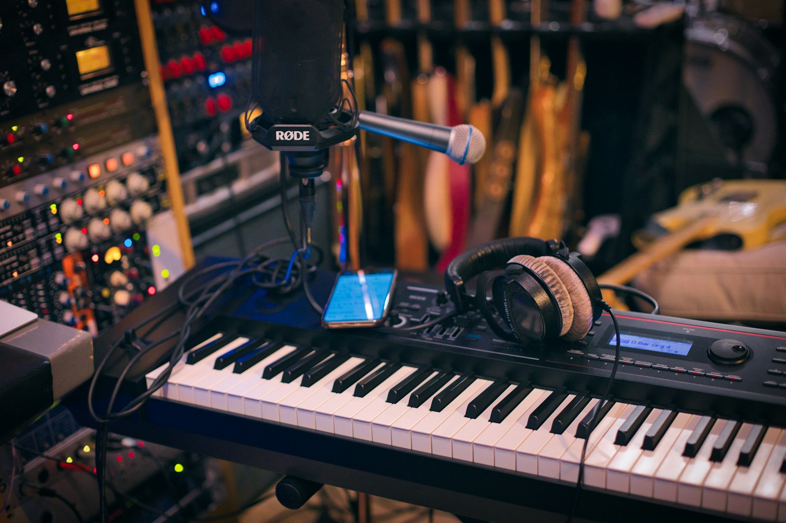 A professional music producer sits in a home studio playing a MIDI keyboard controller while looking at a DAW on a computer screen.
