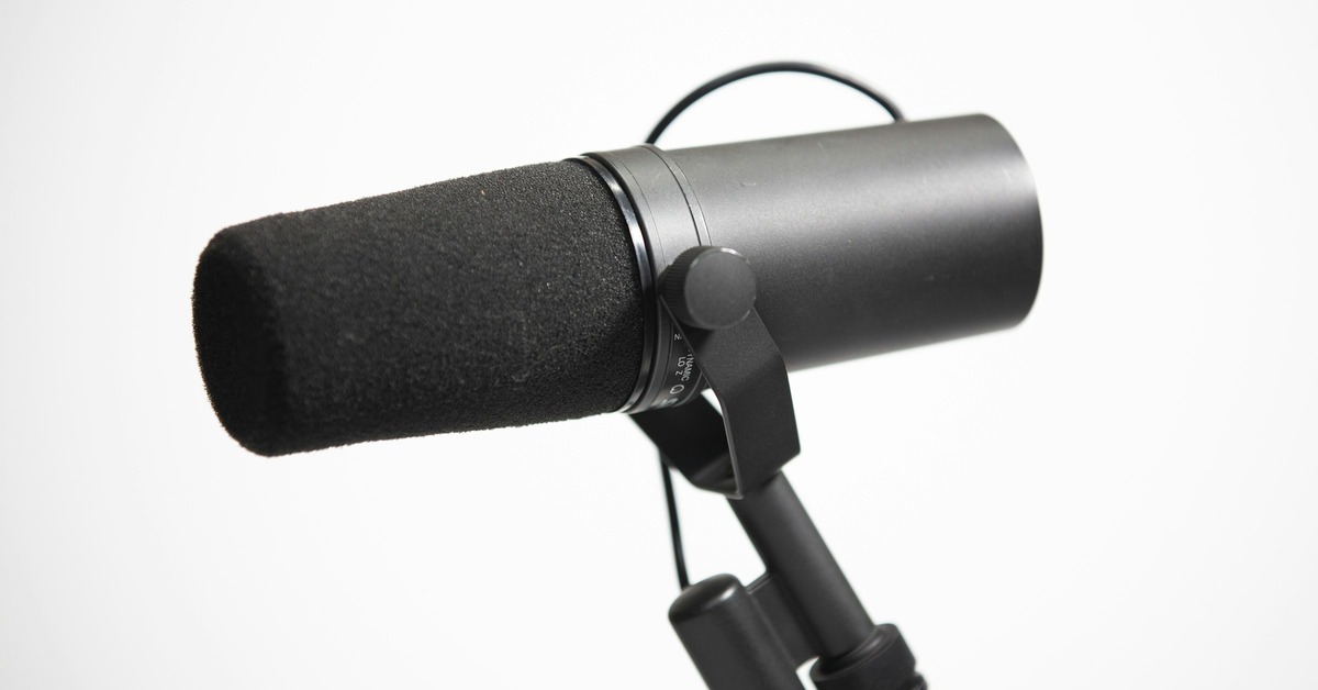 Shure SM7B dynamic microphone and Rode NT1-A condenser microphone placed side by side on a desk in a home studio setup with audio interface in the background.