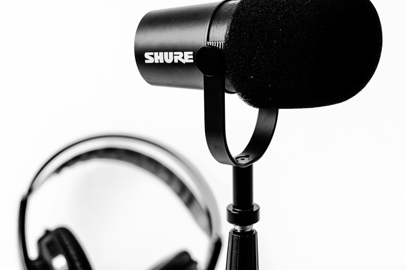 Close up of a vocalist recording into a Shure SM7B microphone mounted on a boom arm in a home studio with sound panels on the wall.